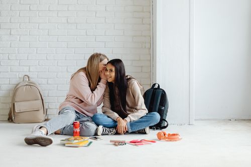 Free Two teenage girls sitting on the floor, whispering and smiling together. Stock Photo
