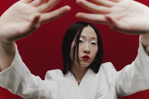 Free A fashionable portrait of an Asian woman in a white blazer, striking a pose against a red background. Stock Photo