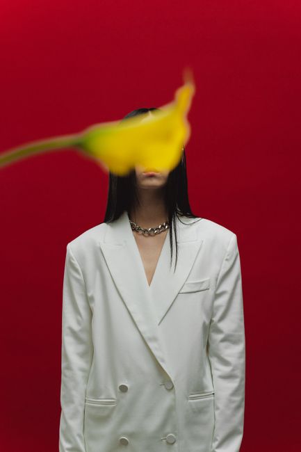 Creative portrait with a white blazer, flower in focus against a bright red backdrop