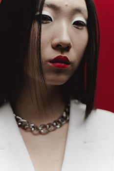 Close-up portrait of a woman with bold red lips, chain necklace, and striking eyeshadow.