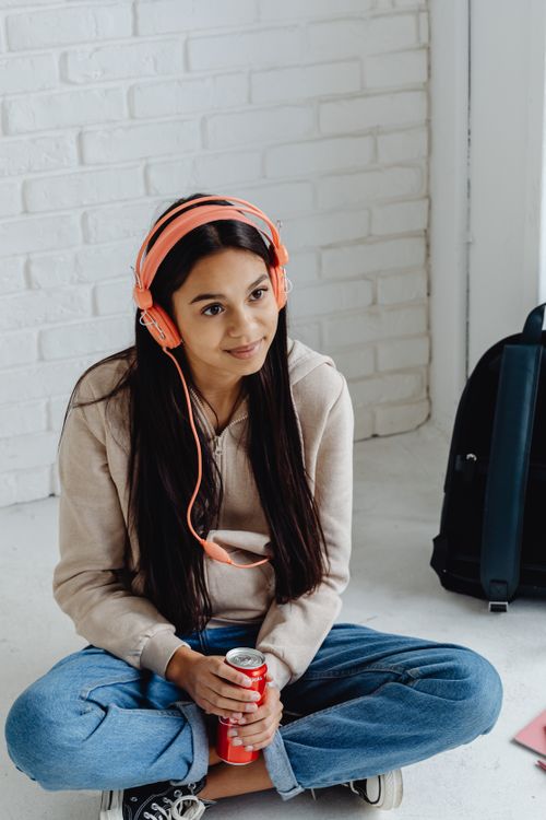 Free Teen girl sitting with headphones on, listening to music and smiling, shows youthful relaxation. Stock Photo