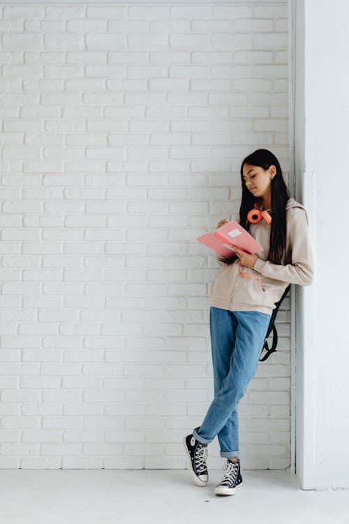 Female Teenager Writing on Her Notebook while Leaning on the Wall