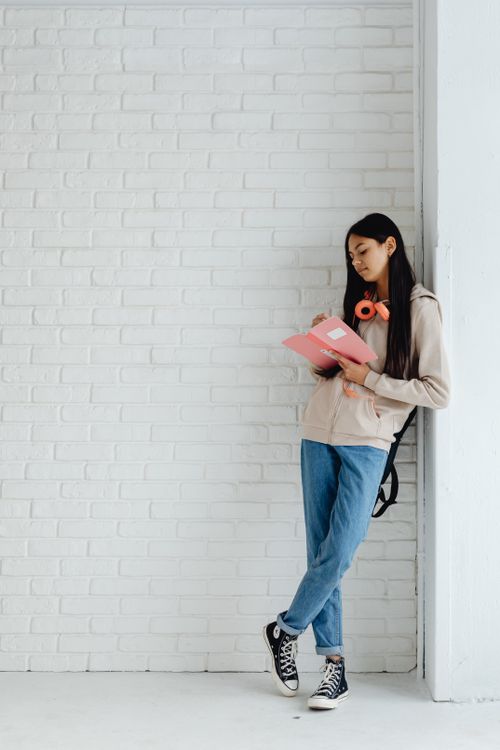 Free Teenage girl with headphones, writing in notebook against a white brick wall. Stock Photo