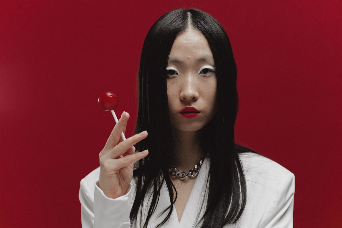 Captivating portrait of an Asian woman with red lips holding a lollipop, set against a striking red background.