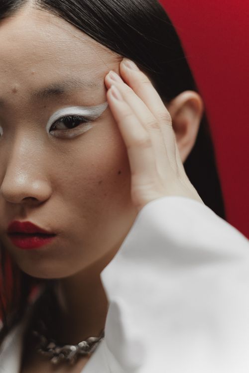 Free An artistic portrait of a woman with striking makeup against a red background. Stock Photo