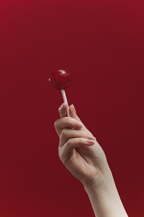 A Hand Holding a Lollipop Near Red Background