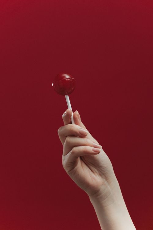 Free A close-up of a hand holding a red lollipop on a matching red background. Stock Photo