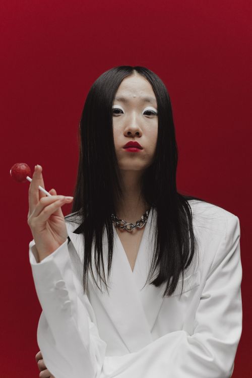 Free Stylish portrait of a woman in a white blazer with a red background, holding a lollipop. Stock Photo