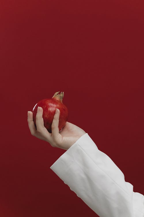A Person in White Long Sleeves Holding a Pomegranate Fruit