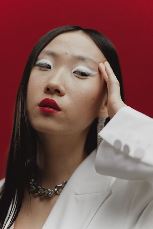 Free Elegant woman wearing white blazer posing against a red background. Stylish and serious. Stock Photo