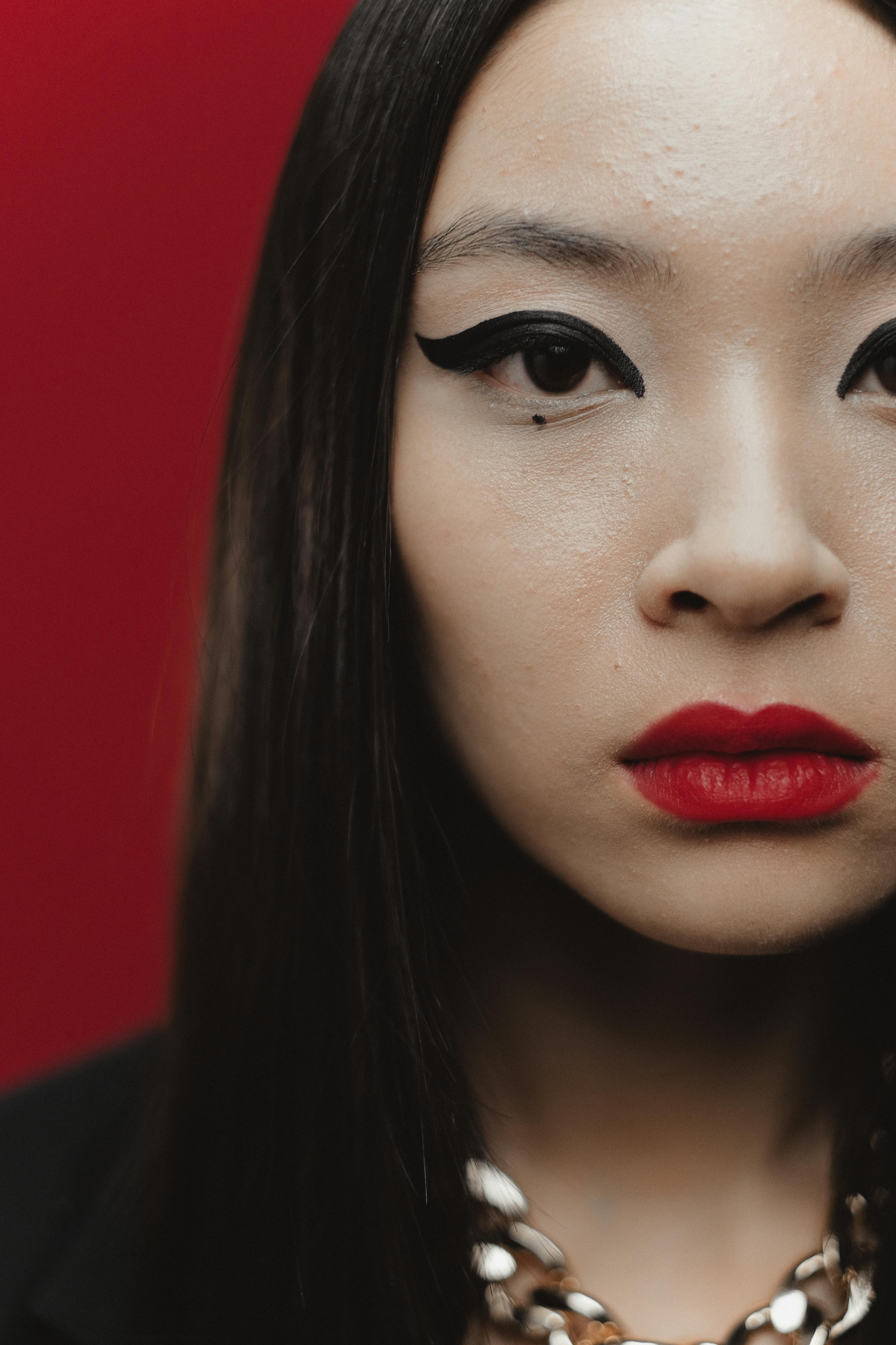 Close-up portrait of a woman with dramatic eye makeup against a vivid red background.