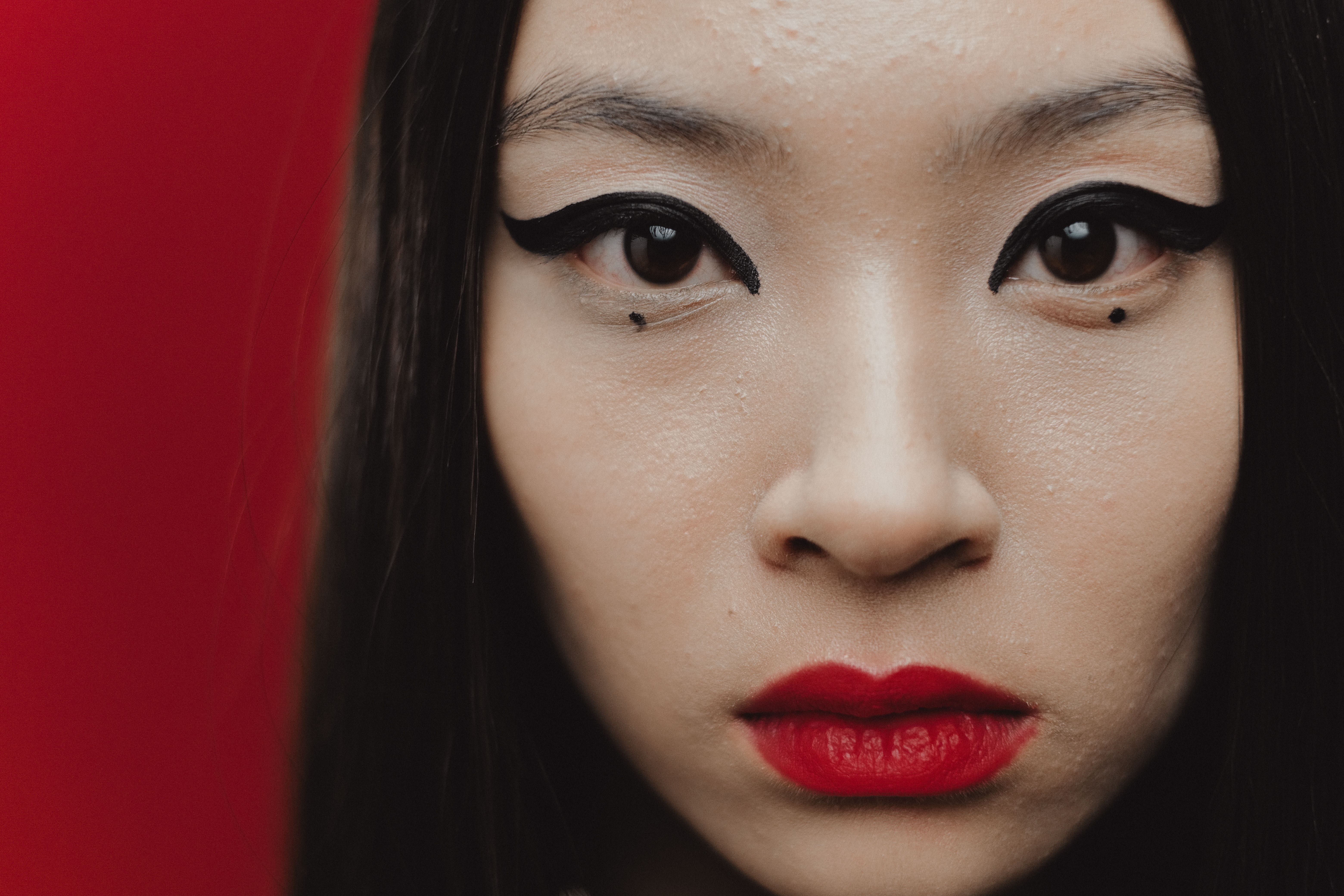 Intense close-up portrait of an Asian woman with striking eyeliner and red lipstick.