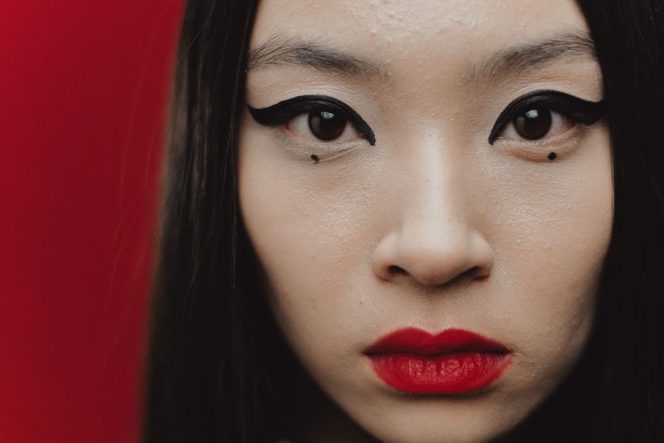 Intense close-up portrait of an Asian woman with striking eyeliner and red lipstick.