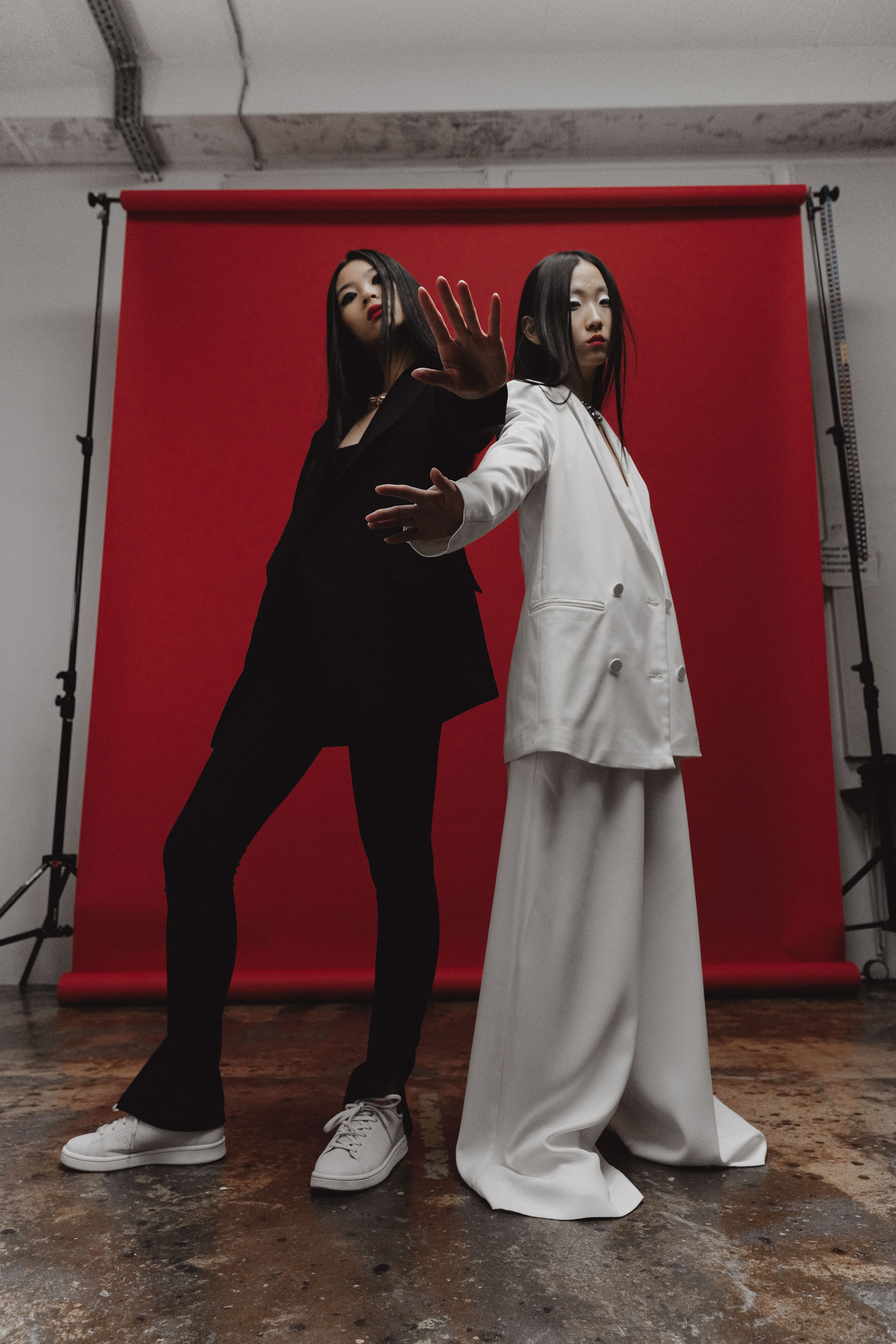 Striking image of two women posing in stylish attire against a bold red background, showcasing modern fashion.