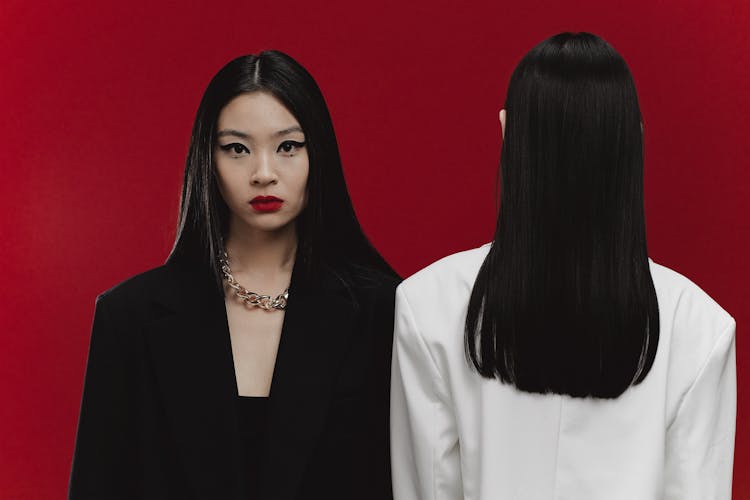 A Woman In Black Blazer Standing Beside The Woman Facing The Red Wall