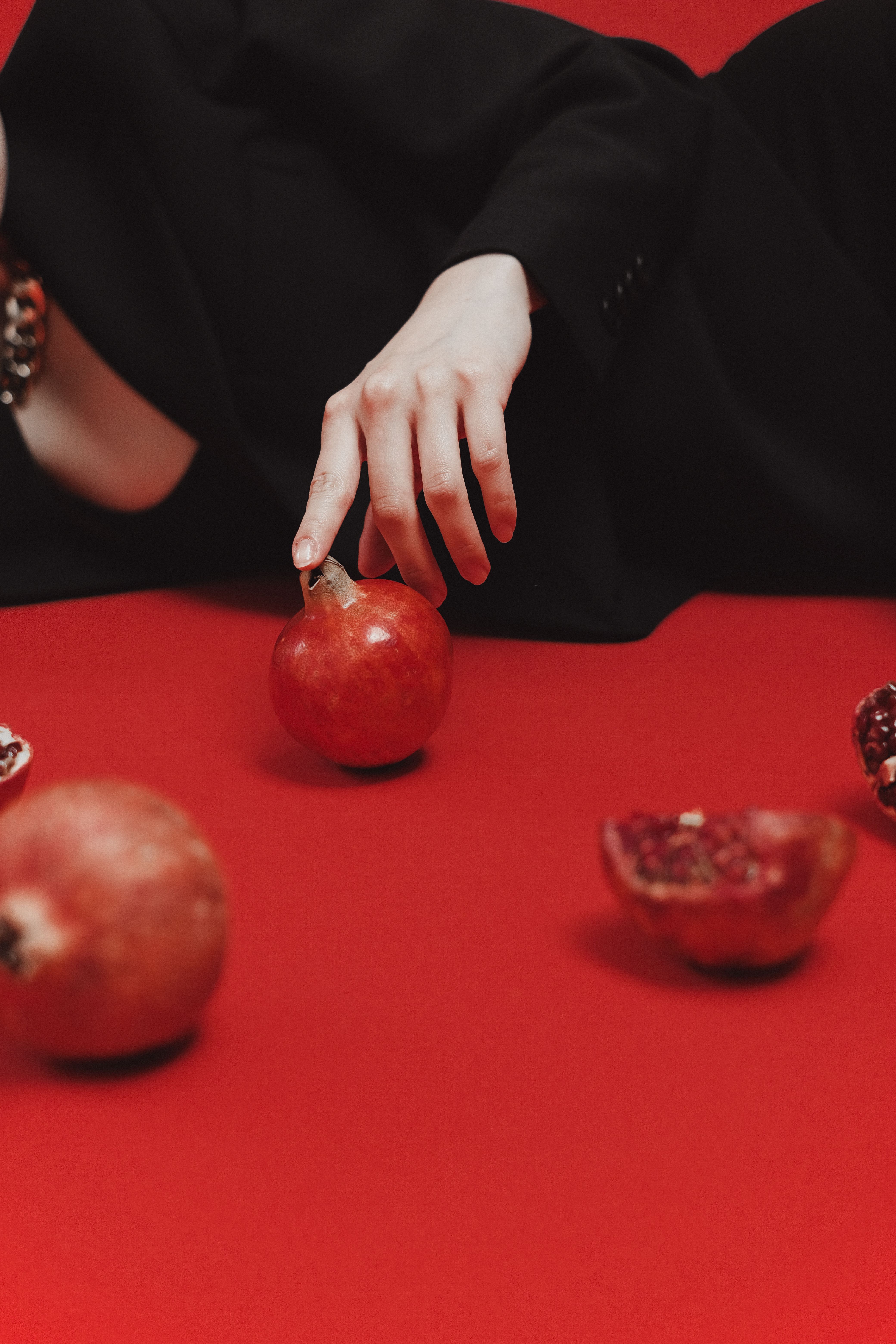 A hand reaches for a pomegranate on a vibrant red surface, creating an artistic still life.