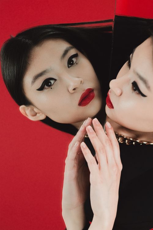 Free Stylish portrait of a woman with bold makeup and mirror reflection against a red background. Stock Photo