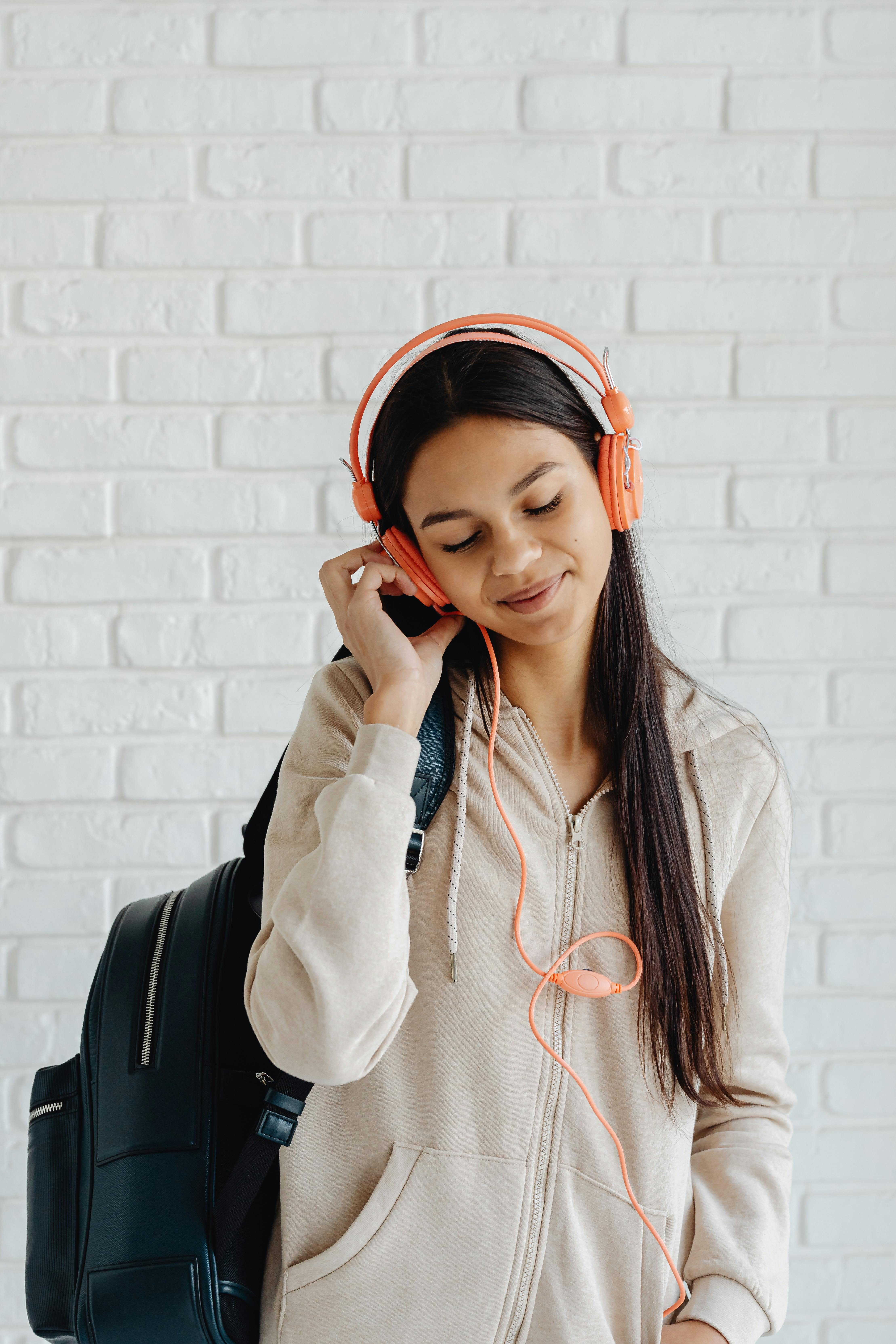 girl in beige hoodie and black backpack holding orange headphones