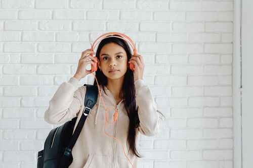 Free Teen girl wearing headphones and a backpack against a brick wall background. Stock Photo
