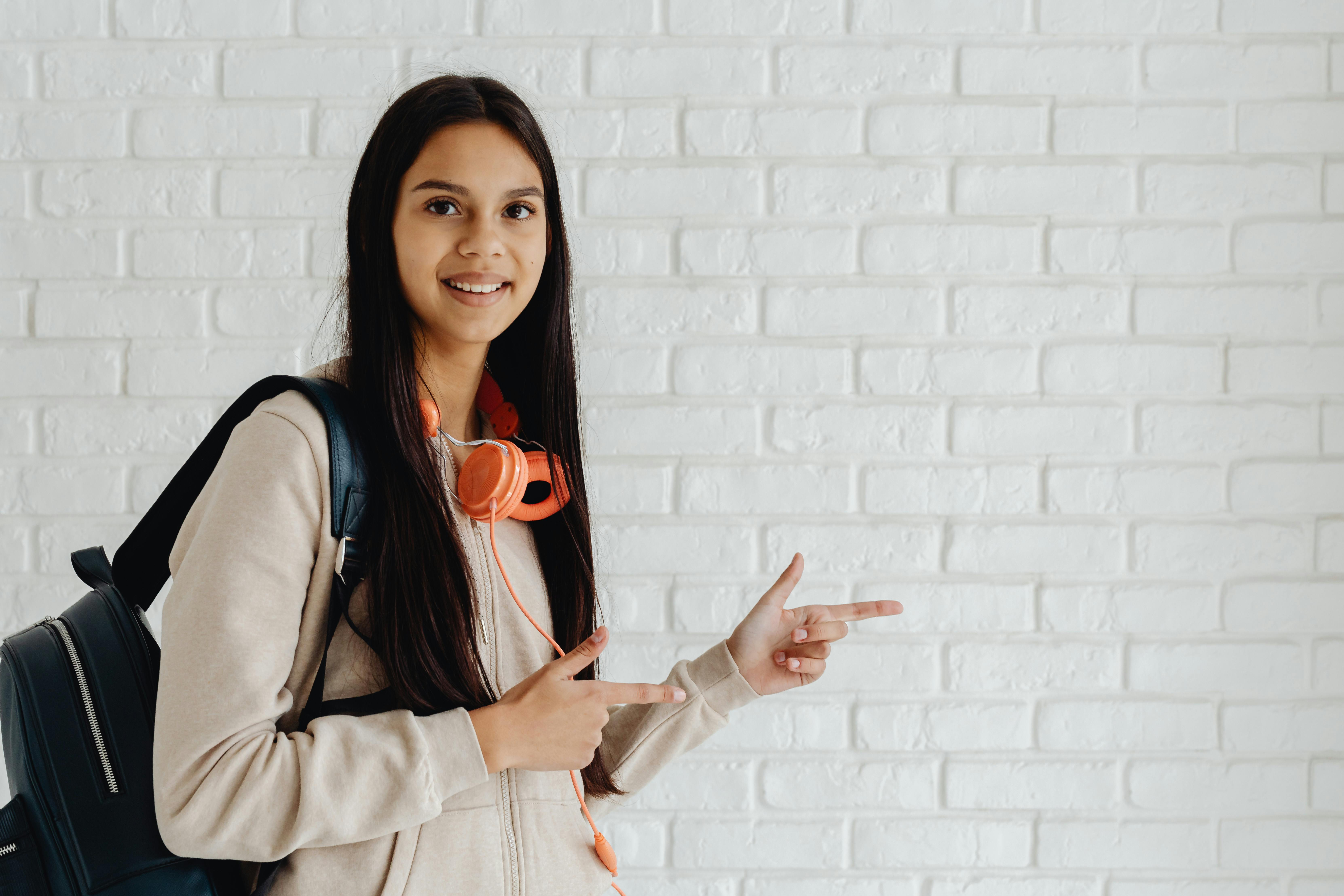 smiling girl in beige hoodie and black backpack pointing fingers