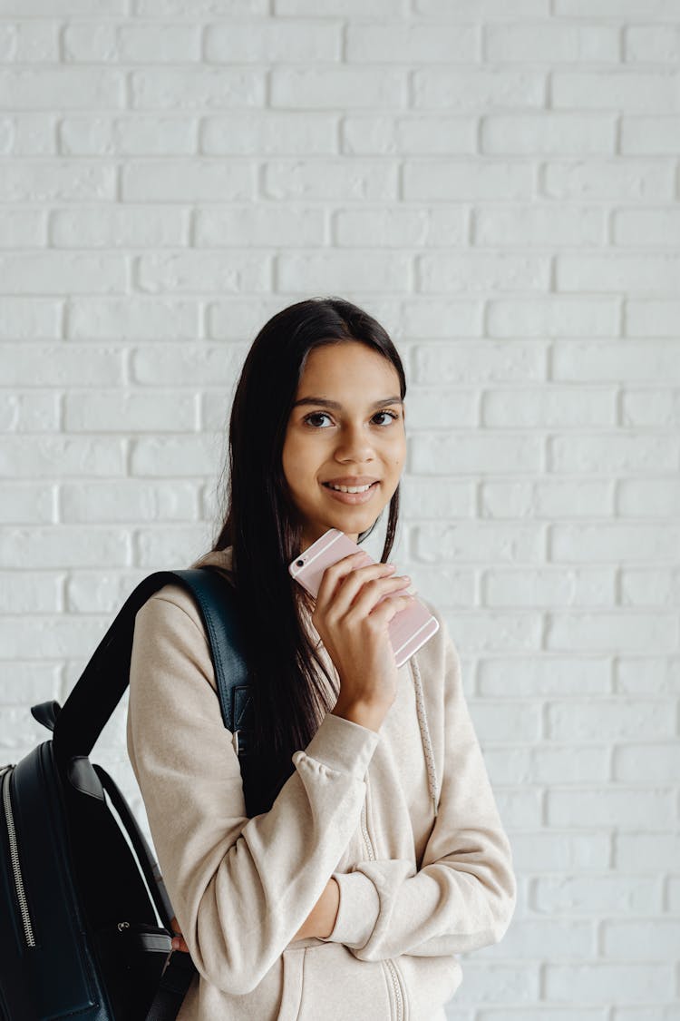 A Lady Smiling At The Camera While Holding Her Phone