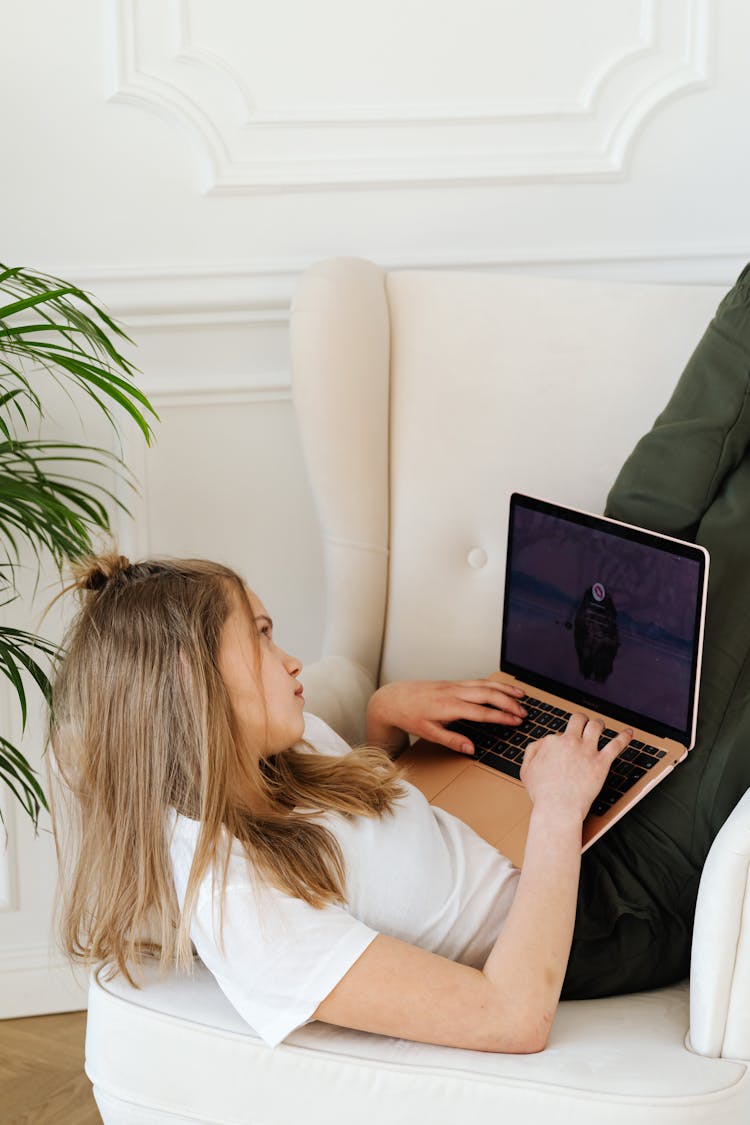 A Lazy Woman Lying On Sofa Chair While Browsing Her Laptop