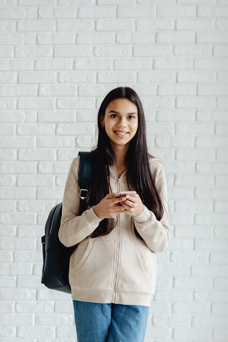 Medium Shot Of A Lady Smiling At The Camera While Holding Her Phone