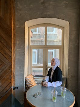 Woman in hijab enjoying coffee by a window in an Istanbul cafe, capturing a serene moment.