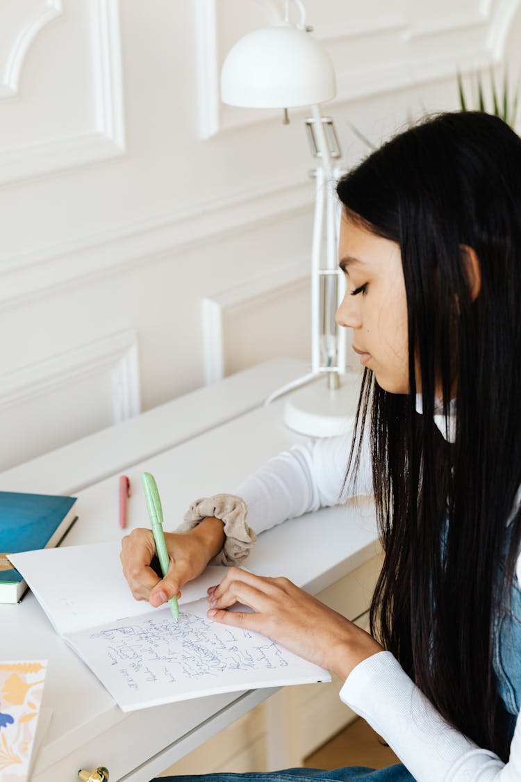  A Woman With Black Hair Writing On A Notebook