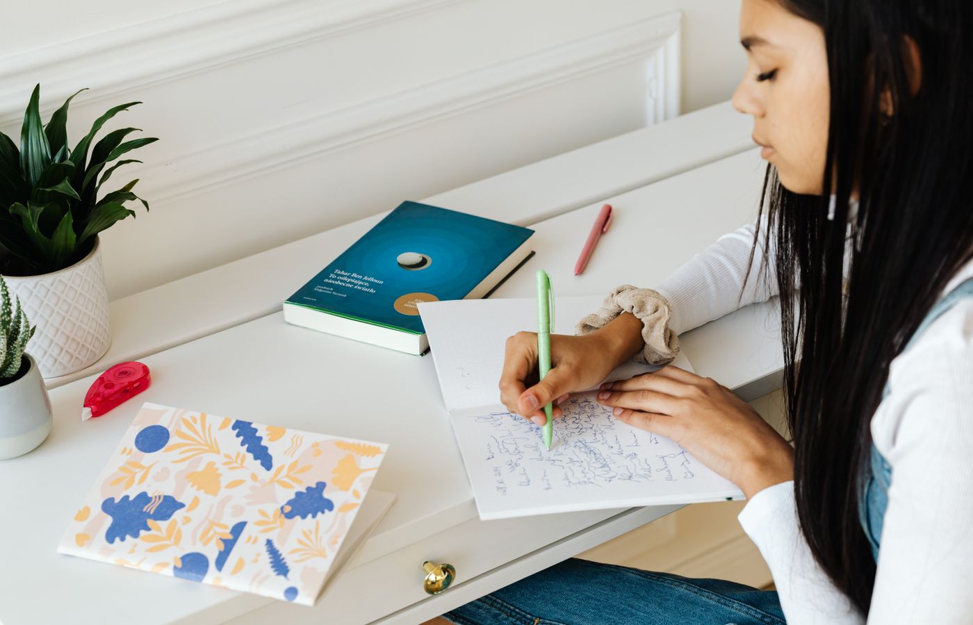 Teenager writing in notebook at home desk, working on school assignments with focus.