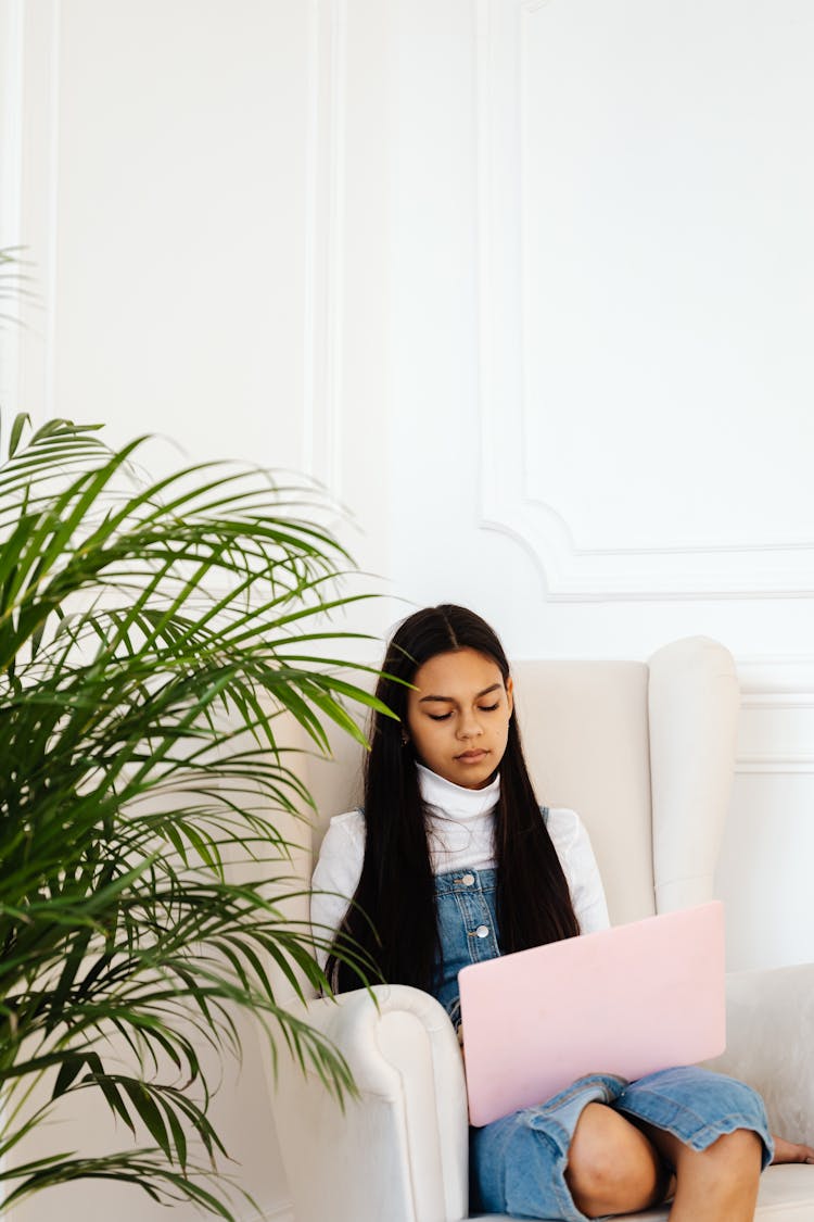 Female Teenager Sitting On An Armchair While Using A Laptop