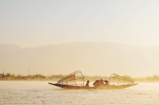 Traditional fishermen in Myanmar on Inle Lake during a serene sunrise with morning fog.
