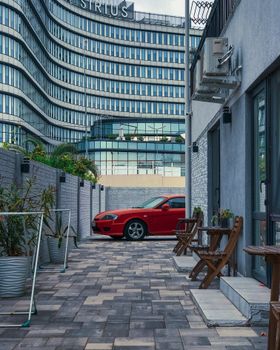 A vibrant red car parked in an urban alley beside modern architecture, hinting at a bustling city vibe.