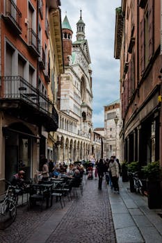 A bustling street in Cremona, Italy, with outdoor cafes and the cathedral in view.
