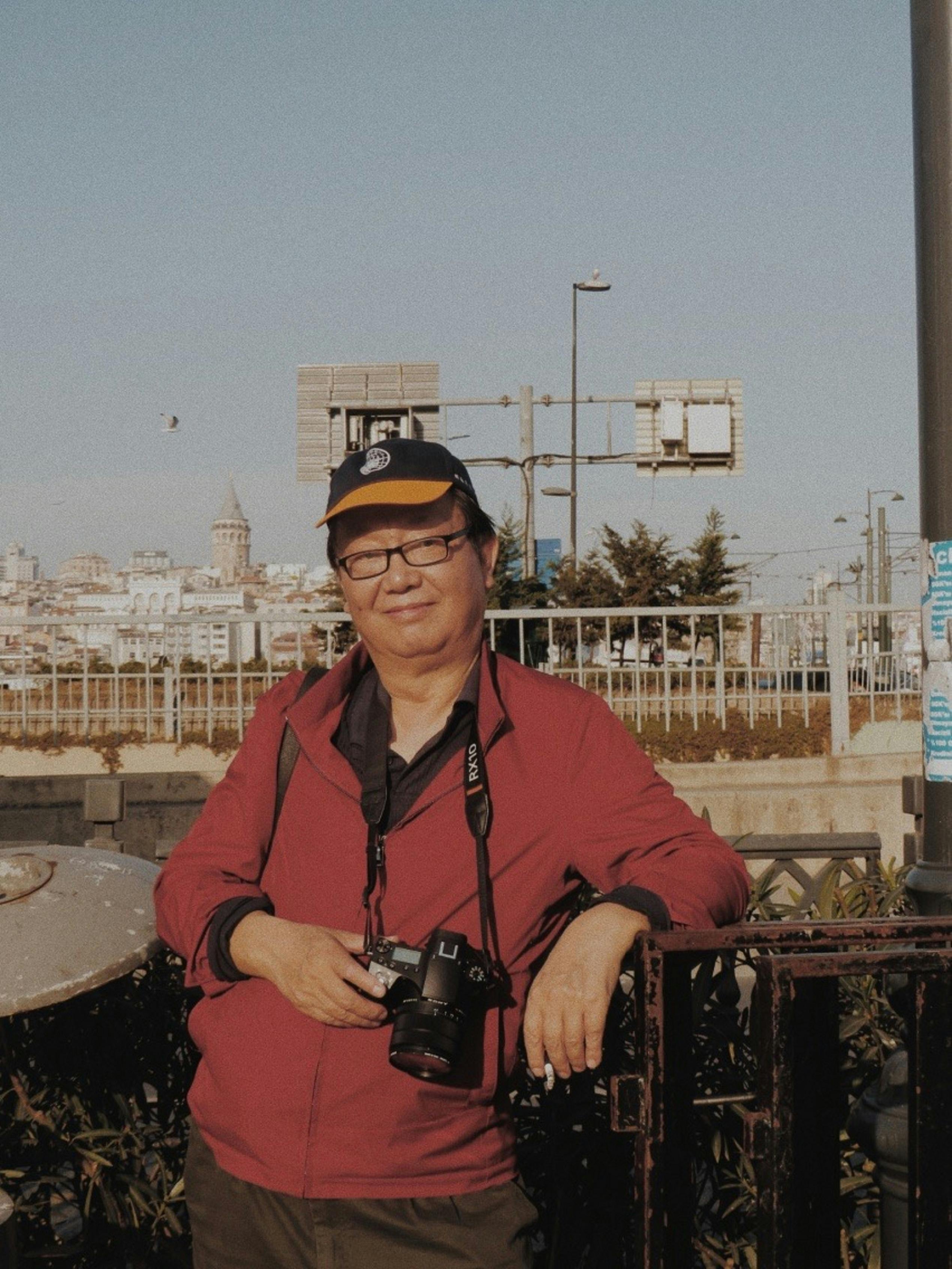 Man with camera stands on a city bridge with a scenic urban backdrop.