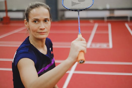 Focused female badminton player ready to hit, on a vibrant red indoor court.