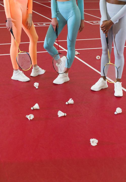 Free Three women holding badminton rackets in activewear on a red court with shuttlecocks. Stock Photo