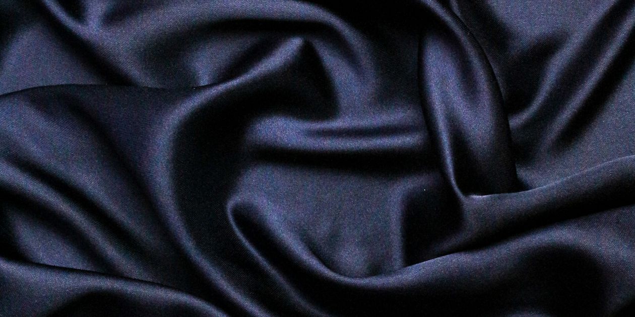 Cận cảnh vải satin đen với các nếp gấp lớn phản chiếu ánh sáng, minh họa độ bóng đặc trưng của mặt vải dệt vân đoạn