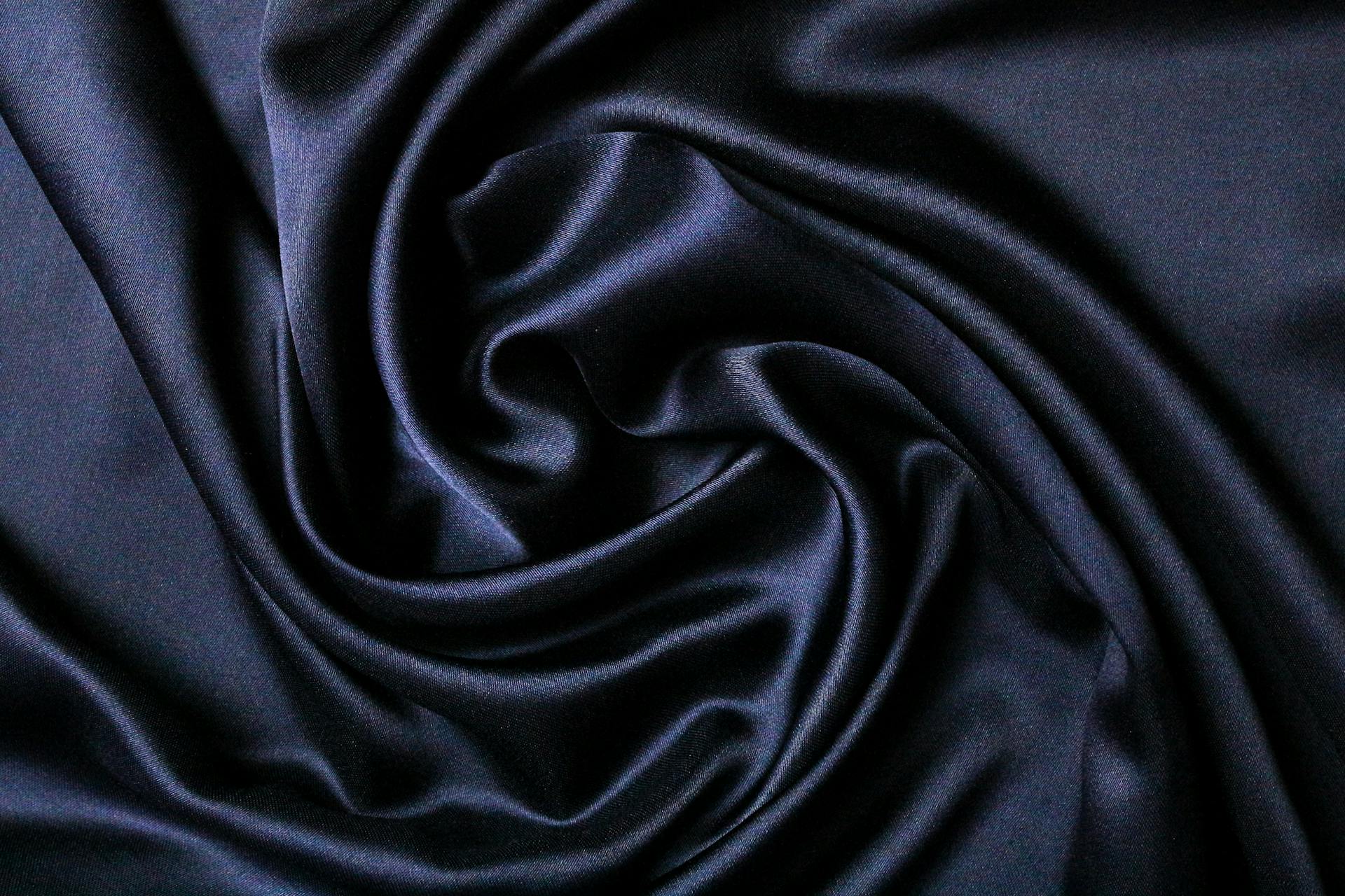 Close-up of smooth black satin fabric with elegant folds creating a luxurious texture.