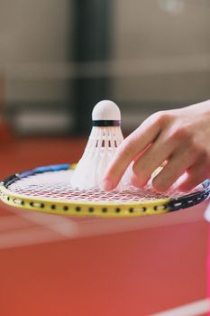 Close-up of a hand placing a shuttlecock on a badminton racket indoors.