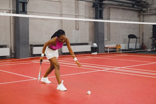 Young African American woman playing badminton indoors, reaching for a shuttlecock on a red court.