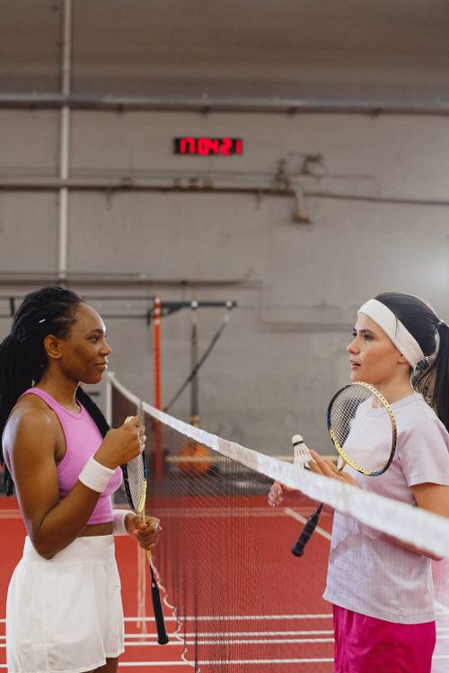 Free Two women interacting on a badminton court wearing activewear, holding rackets. Stock Photo