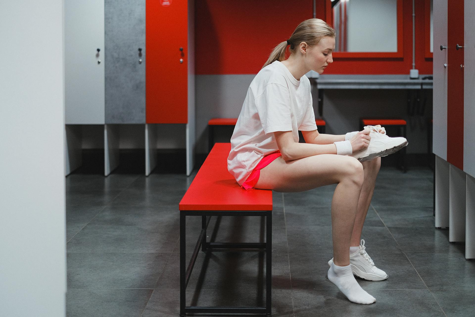Young woman in activewear sitting in a locker room tying her shoes, ready for a workout.