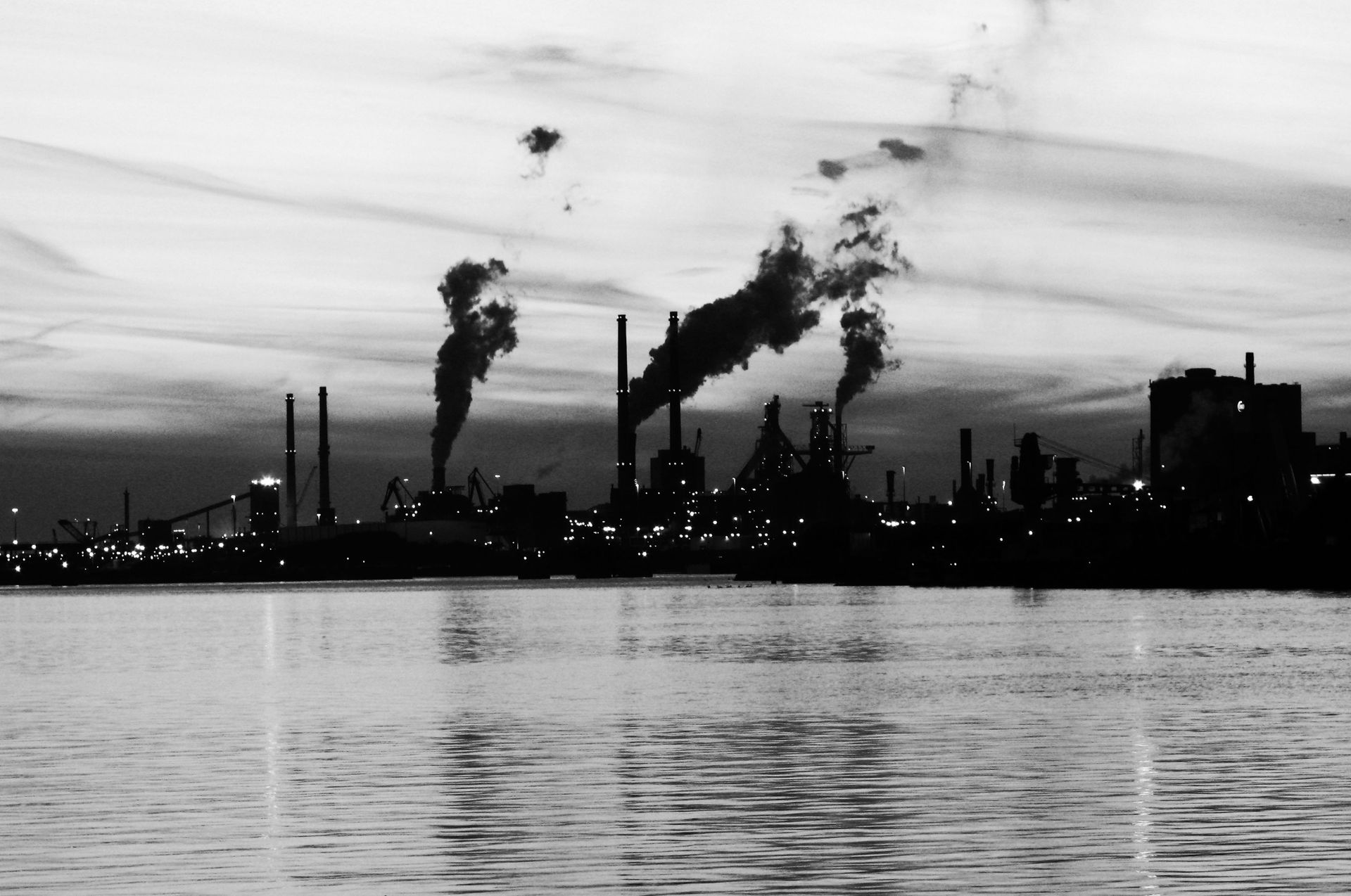 Dramatic industrial cityscape with smokestacks silhouetted against the twilight sky.