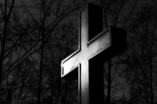 Black and white image of a tall cross standing against forest trees, exuding a dramatic and moody feel.