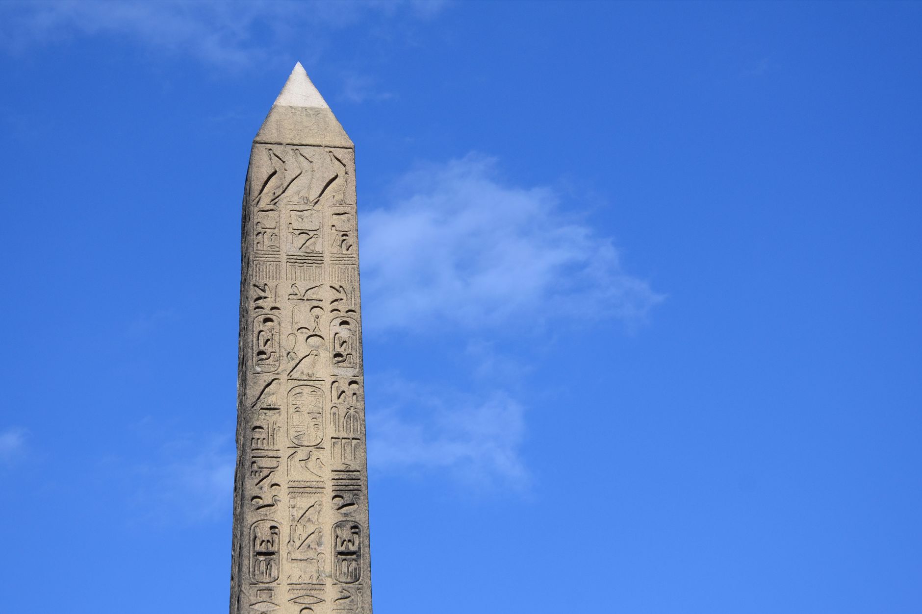 Close-up of an ancient obelisk with hieroglyphs set against a bright blue sky.
