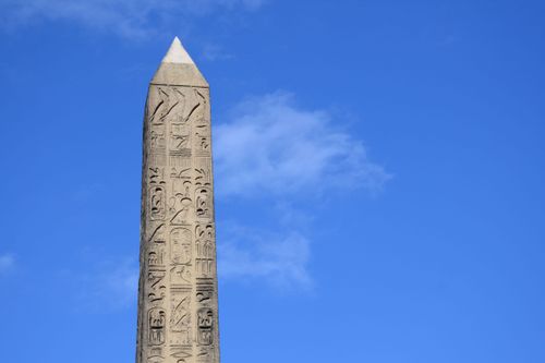 Free Close-up of an ancient obelisk with hieroglyphs set against a bright blue sky. Stock Photo
