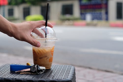 A Person's Hand Holding Clear Plastic Cup With Coffee