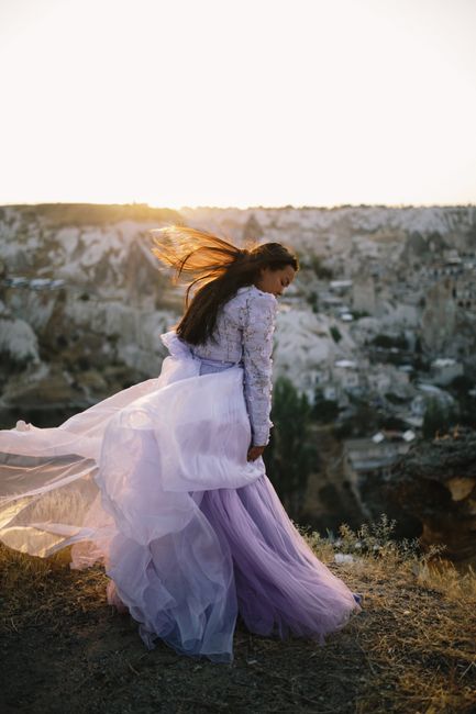 A woman in a purple dress stands on a cliffside with the wind blowing at sunset, capturing elegance and freedom.