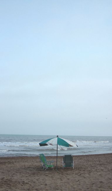 Fotomural Un escenario de playa pacífico con un paraguas y sillas en la arena, con olas al fondo.